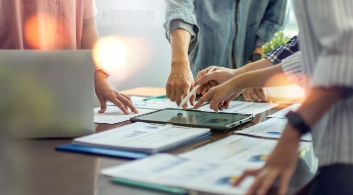 Photo of people gathered around a table pointing at papers